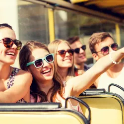 a group of teens on a bus smiling and pointing to something interesting outside the window. 