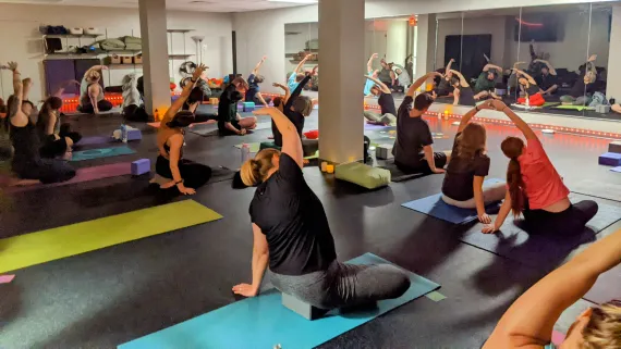 a group of students performing a yoga pose with their arms as they sit on their mats. 