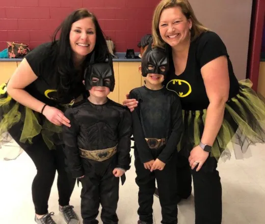 Two moms dressed up as Bat Girl, with their sons who are both dressed as Batman