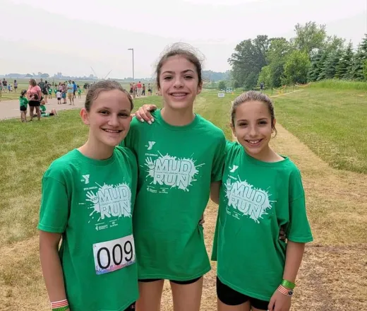 three young girls wearing YMCA t-shirts smiling at the annual kids mud run.