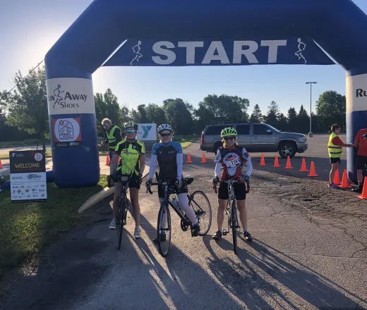 a group of people on their bikes smiling by the start line of the Oshkosh century ride.