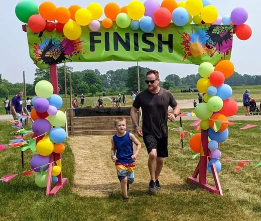 a father and son running through the finish line full of balloons at the mud run.