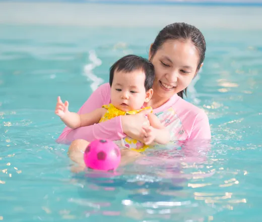 a mom and her infant daughter playing in the pool with floaty toys.
