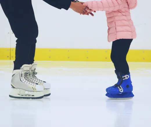 a child holding hands with a skate instructor in the ice arena.