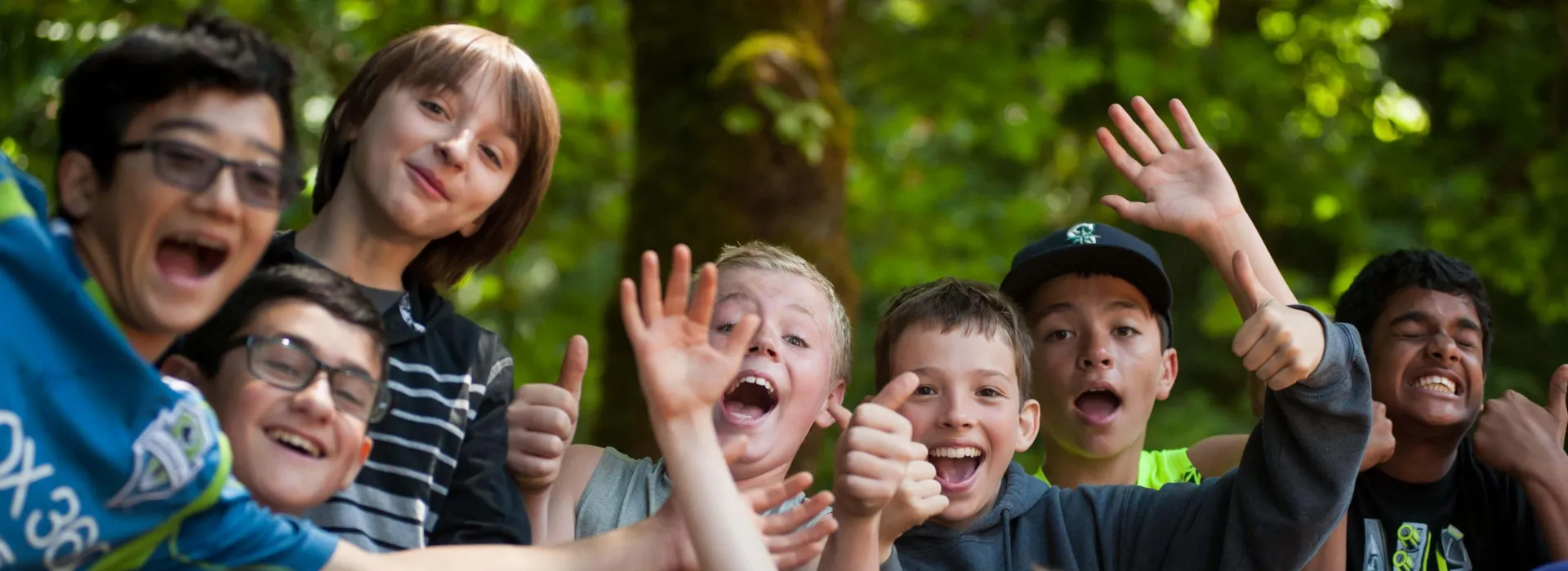 A group of excited young campers waving and giving a thumbs up.