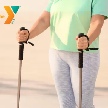 A close up shot of a woman in work out leggings with a walking pole in each hand.